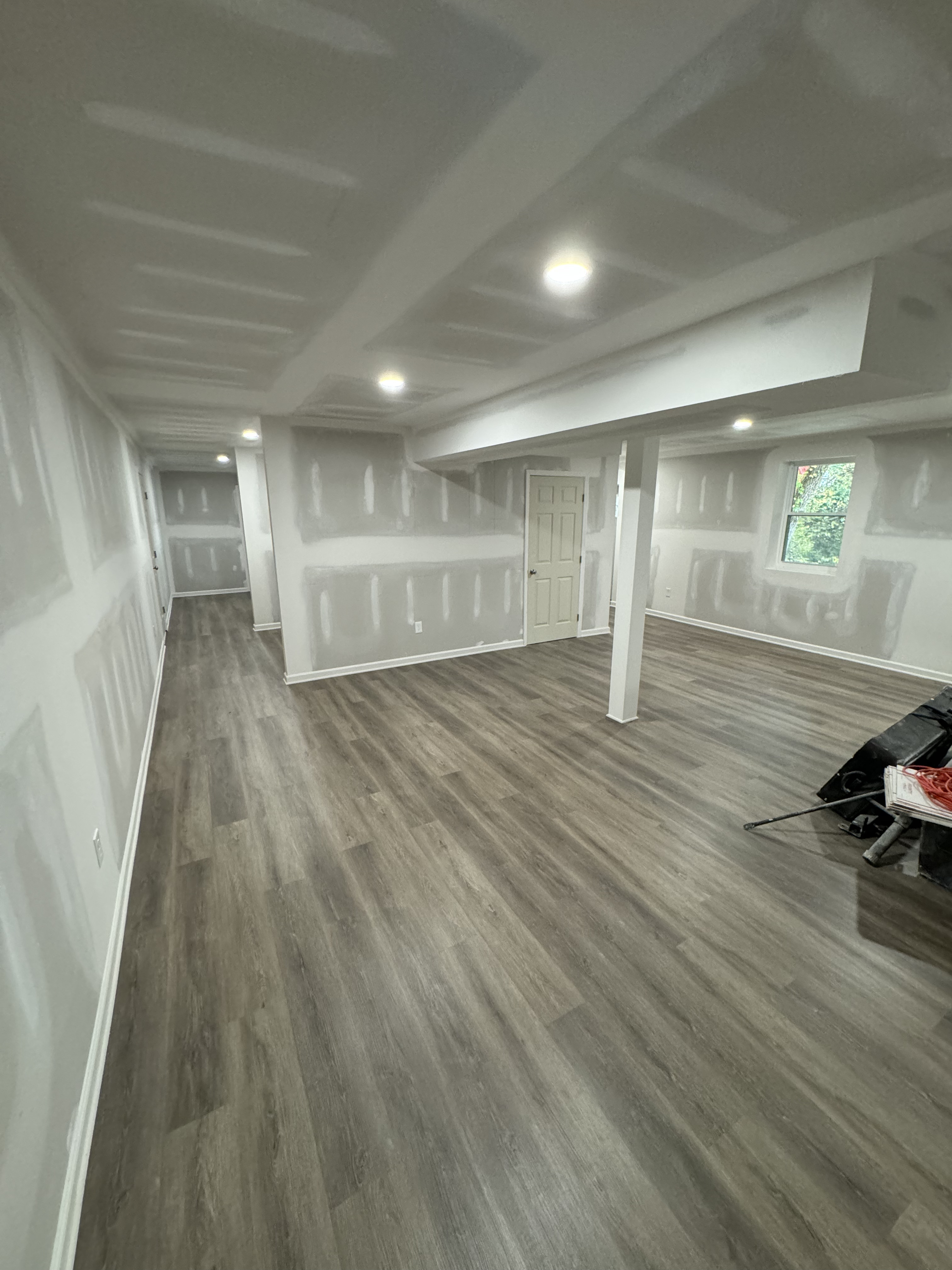 Newly finished basement with fresh drywall, recessed lighting, and gray luxury vinyl plank flooring
