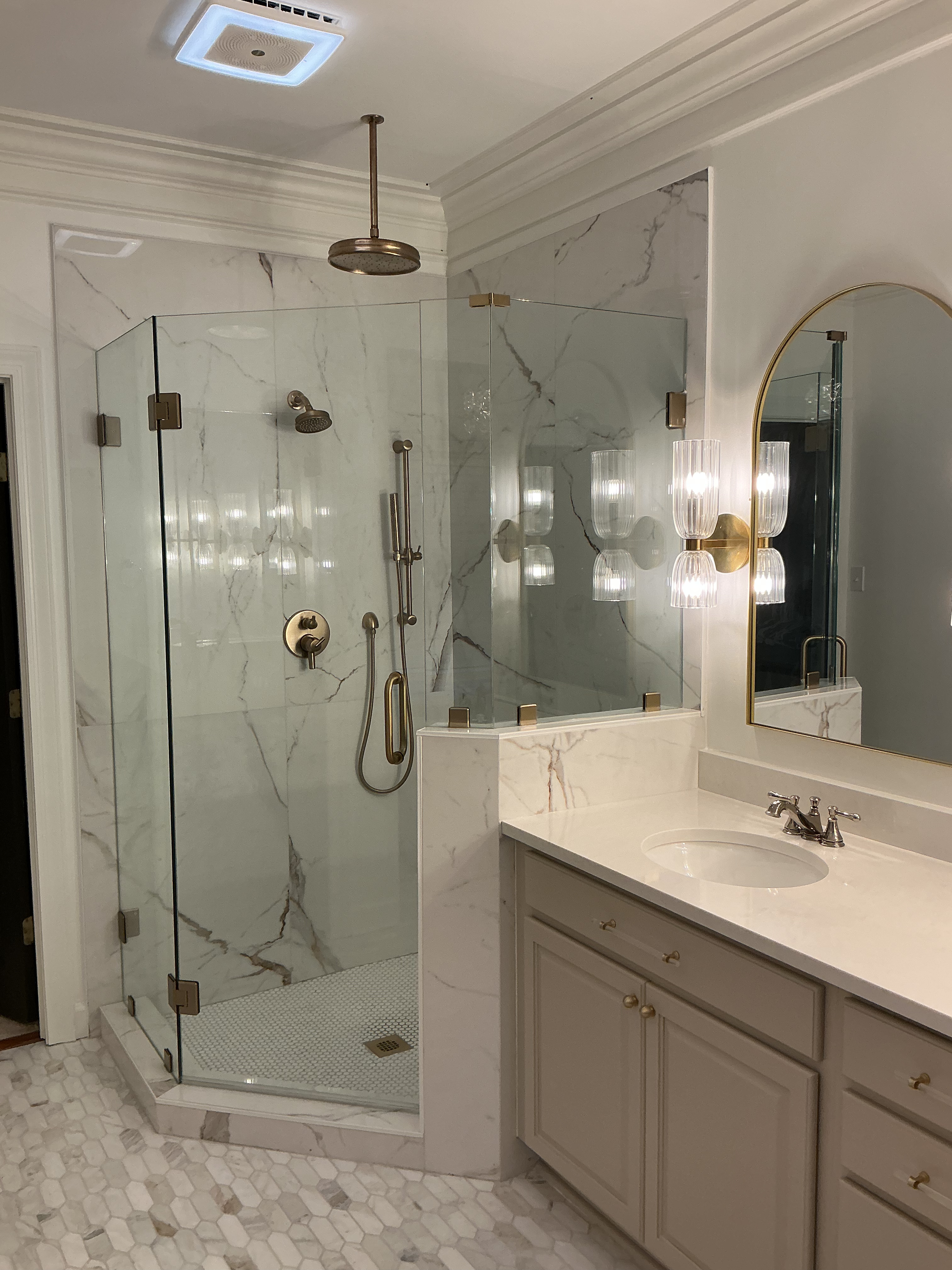 Remodeled bathroom with a marble-tiled glass walk-in shower, brushed-gold fixtures, and a custom vanity