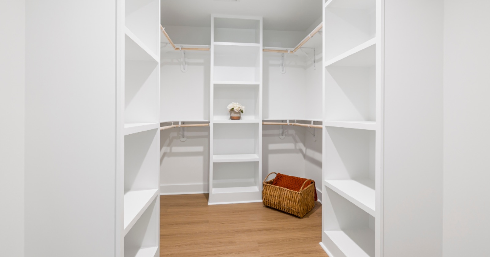Custom walk-in closet upgrade with white built-in shelving, wood rods, drawers, and wood flooring in a Huntsville home