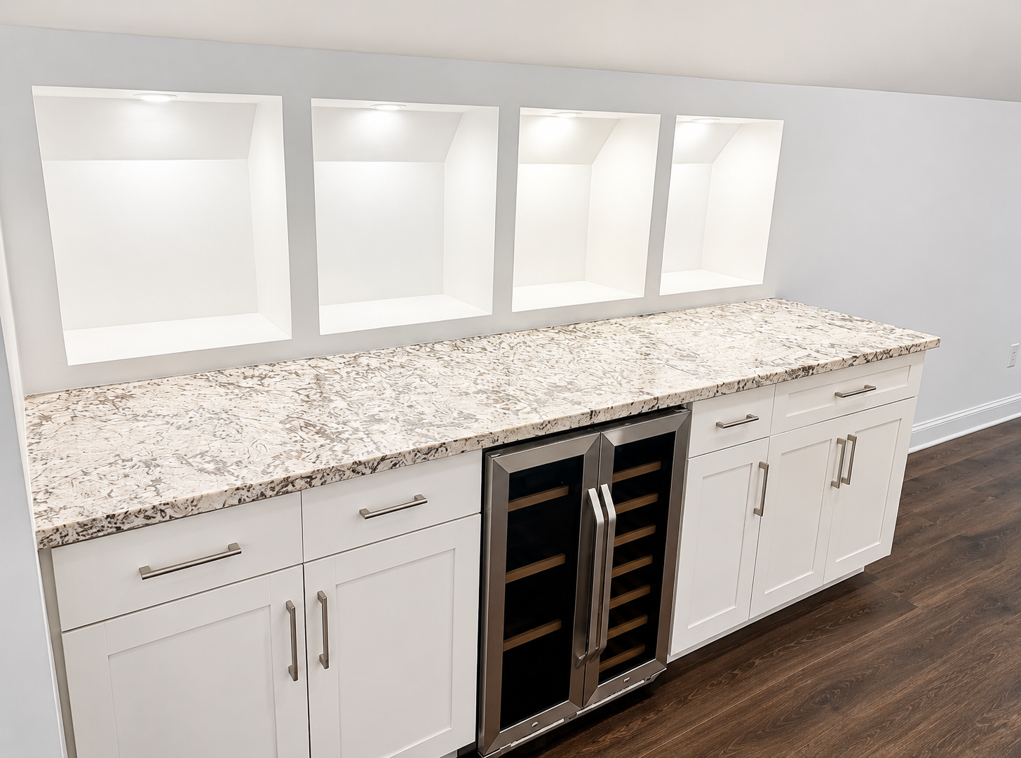 Custom built-in beverage bar with white shaker cabinets, granite countertop, lighted display niches, and a stainless steel wine fridge by Warner's Remodeling